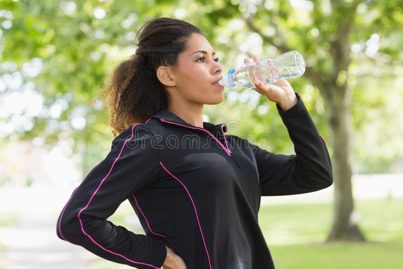 Side view of a tired healthy young woman drinking water in the park. Side view of a tired healthy young woman drinking water in the park