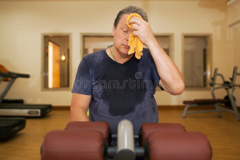 Exhausted mature man wiping sweat with a towel after intensive training in the gym. Exhausted mature man wiping sweat with a towel after intensive training in the gym