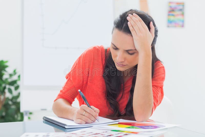 Tired designer holding her head while she is drawing on a notepad. Tired designer holding her head while she is drawing on a notepad