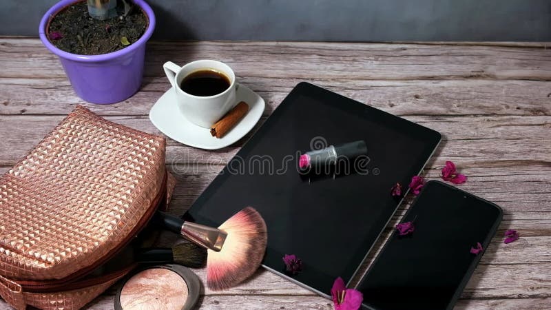 κραγιόν πάνω από ένα δισκίο περιτριγυρισμένο από ένα καπνιστό φλασκί καφέ smartphone και μακιγιάζ. με τη βροχή της όρασης petalsto