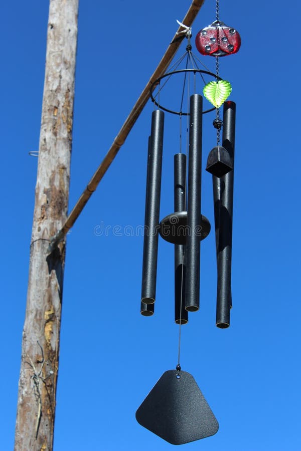 Two wind chimes on a wood post with a bright blue sky background. Two wind chimes on a wood post with a bright blue sky background.