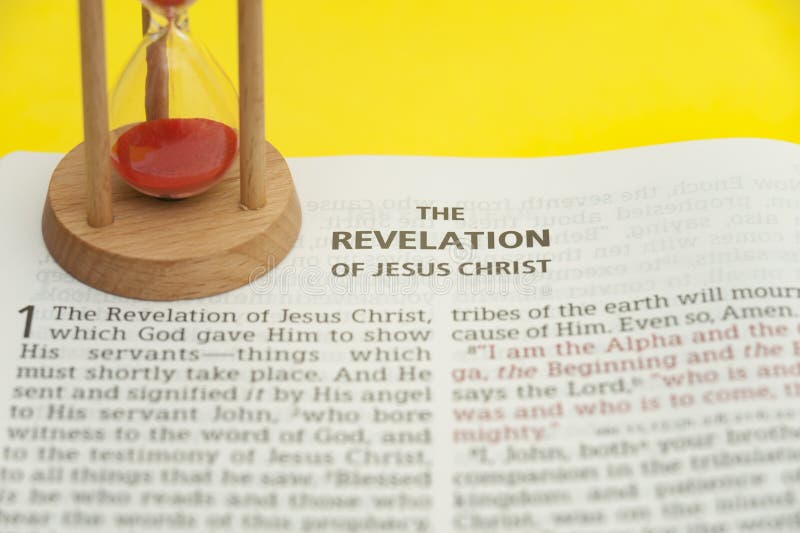 Red sand hourglass on top of open Holy Bible in the Book of Revelation of Jesus Christ chapter 1. Isolated on yellow background. Close-up. Horizontal shot. Red sand hourglass on top of open Holy Bible in the Book of Revelation of Jesus Christ chapter 1. Isolated on yellow background. Close-up. Horizontal shot