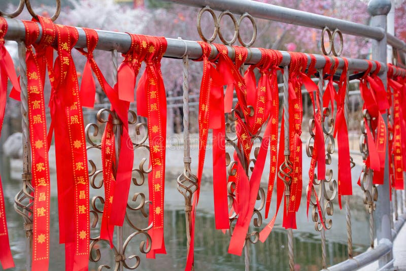 Red ribbon for blessing on the fence. At the Yuquan Mountain Cherry Blossom Festival in Taiyuan, Shanxi, China, the iron fence of the pond is covered with red ribbons with Chinese characters used to pray for peace, health, wealth, and a vision for a better life.Red ribbon in front of cherry blossom background. Red ribbon for blessing on the fence. At the Yuquan Mountain Cherry Blossom Festival in Taiyuan, Shanxi, China, the iron fence of the pond is covered with red ribbons with Chinese characters used to pray for peace, health, wealth, and a vision for a better life.Red ribbon in front of cherry blossom background.