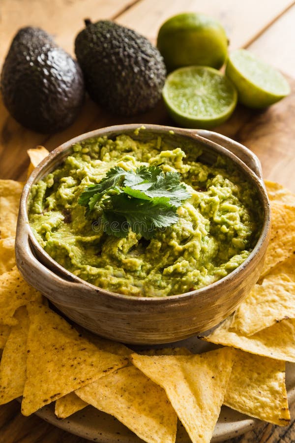 Bowl of guacamole dip with tortilla chips and avocado and limes in the background. Bowl of guacamole dip with tortilla chips and avocado and limes in the background.