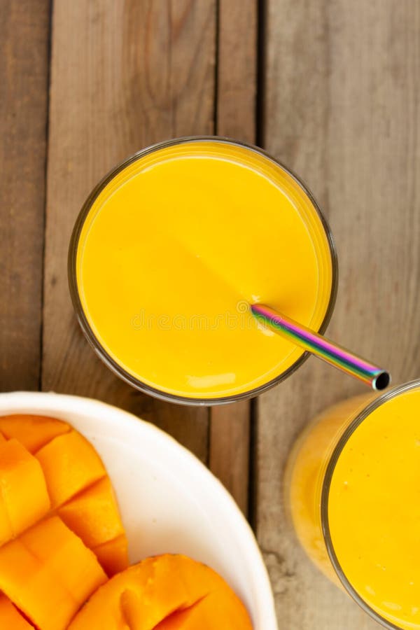 κύρια προβολή mango lassi. ποτό μάνγκο στο γυαλί με πολύχρωμο μέταλλο ή οικολογικό άχυρο. λευκή πλάκα με κομμένο μαντήλι στοκ φωτογραφία