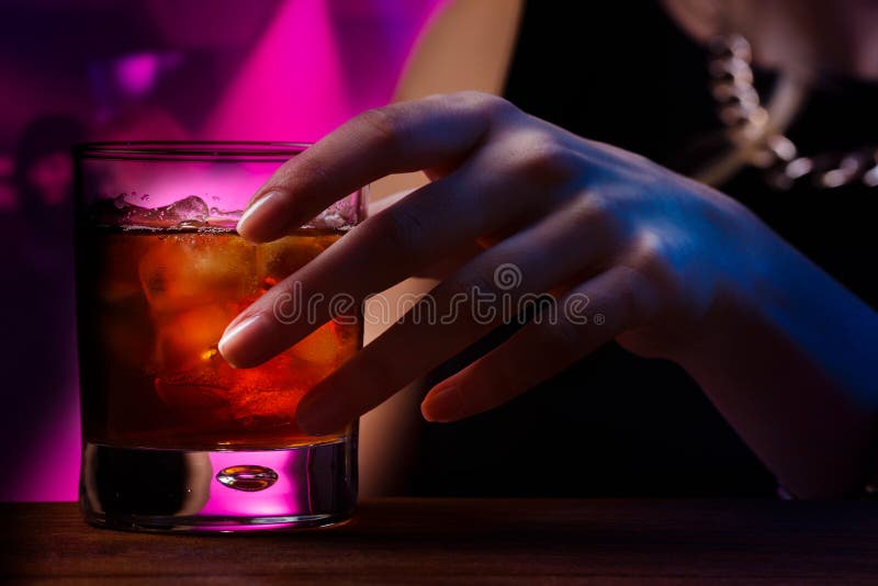 Woman's hand holding old fashioned glass with cold cocktail against blurred night club background. Woman's hand holding old fashioned glass with cold cocktail against blurred night club background