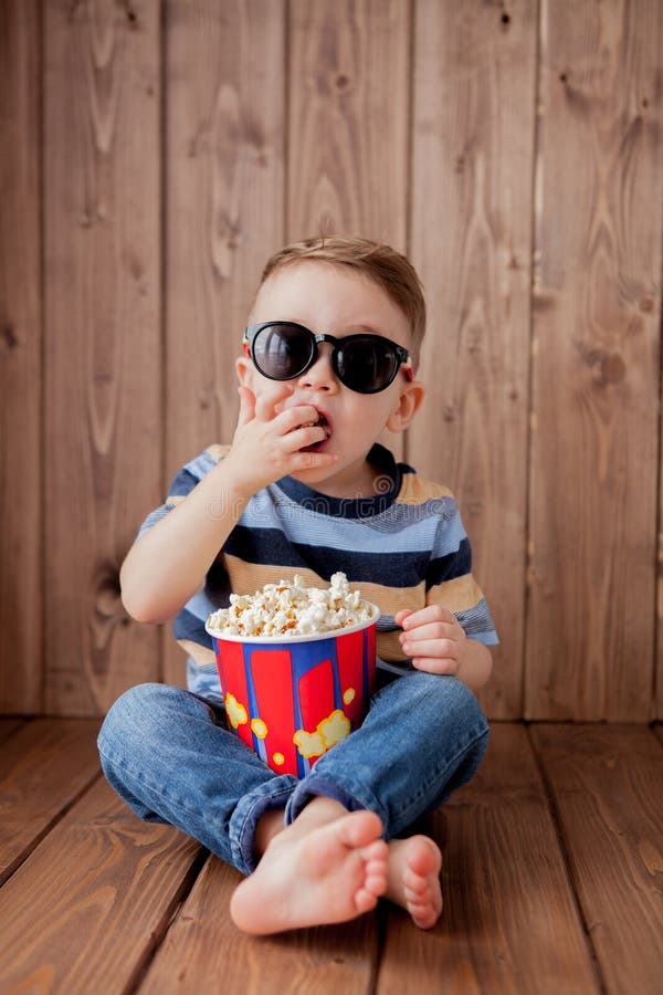 Little cute kid baby boy 2-3 years old , 3d cinema glasses holding bucket for popcorn, eating fast food on wooden background. Kids childhood lifestyle concept. Copy space. Little cute kid baby boy 2-3 years old , 3d cinema glasses holding bucket for popcorn, eating fast food on wooden background. Kids childhood lifestyle concept. Copy space