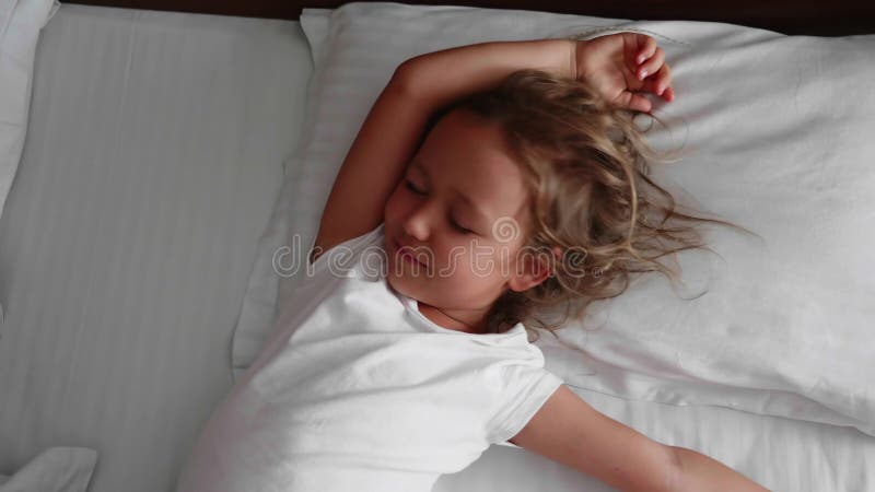 Λίγο χαριτωμένο κορίτσι ξυπνά και τεντώνει στο κρεβάτι στο πρωί