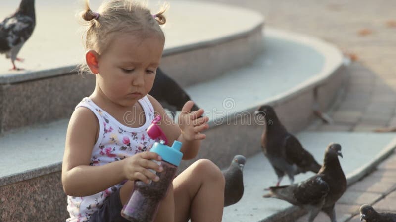 Λίγο χαριτωμένο κορίτσι ταΐζει τα περιστέρια κοντά στην πηγή
