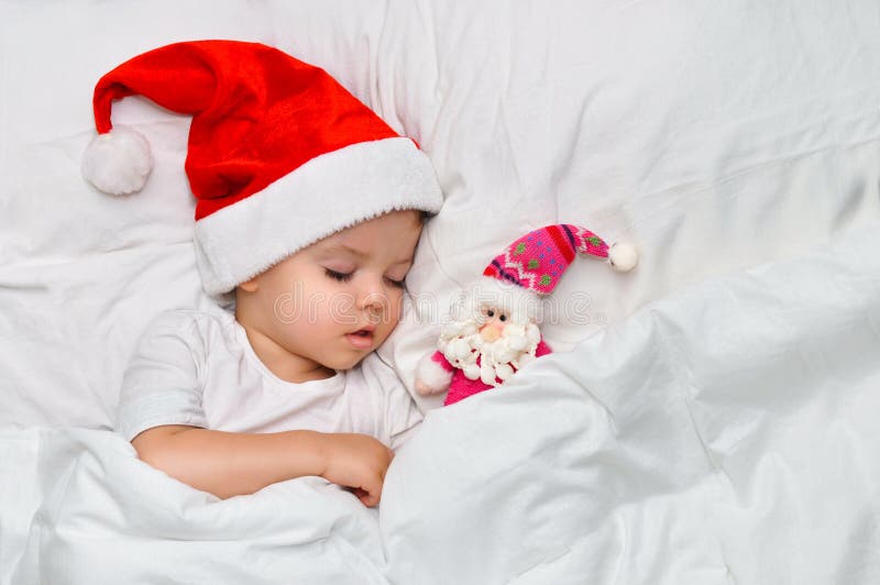 Λίγος ύπνος μωρών στο άσπρο λινό στο καπέλο Santa με το παιχνίδι του Άγιος Βασίλης στοκ εικόνες Λίγος ύπνος μωρών στο άσπρο λινό στο καπέλο Santa με το παιχνίδι του Άγιος Βασίλης στοκ εικόνες
