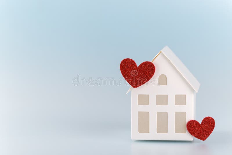 White little toy house with two red hearts on blue background, family concept copy space. White little toy house with two red hearts on blue background, family concept copy space