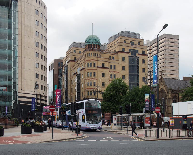 Leeds, west yorkshire, united kingdom - 18 june 2019: buses and pedestrians crossing the road in city square leeds with tall office buildings of park row. Leeds, west yorkshire, united kingdom - 18 june 2019: buses and pedestrians crossing the road in city square leeds with tall office buildings of park row