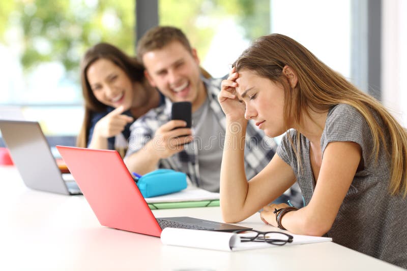 Sad student victim of cyber bullying sitting in a desk in a classroom. Sad student victim of cyber bullying sitting in a desk in a classroom