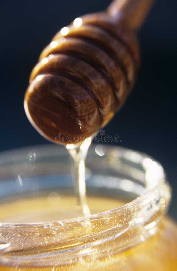 Honey running from wooden honey spoon into honey jar. Honey running from wooden honey spoon into honey jar