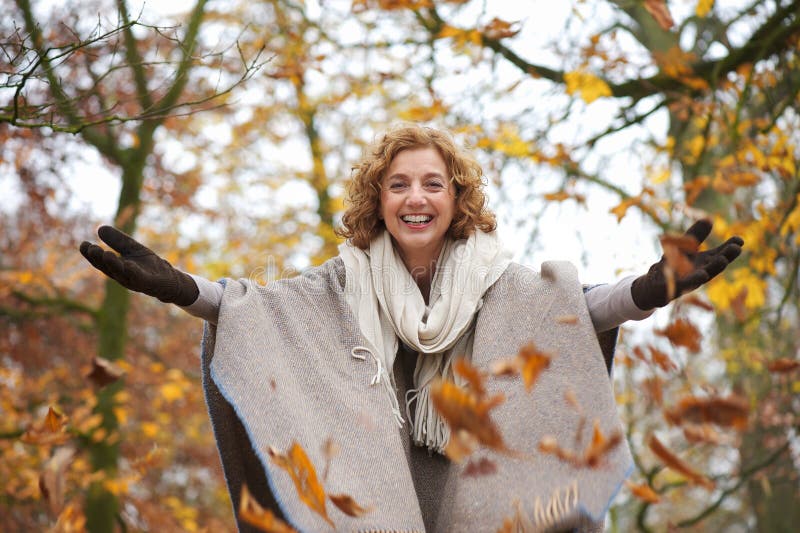 Middle aged woman throwing leaves in autumn with open arms. Middle aged woman throwing leaves in autumn with open arms