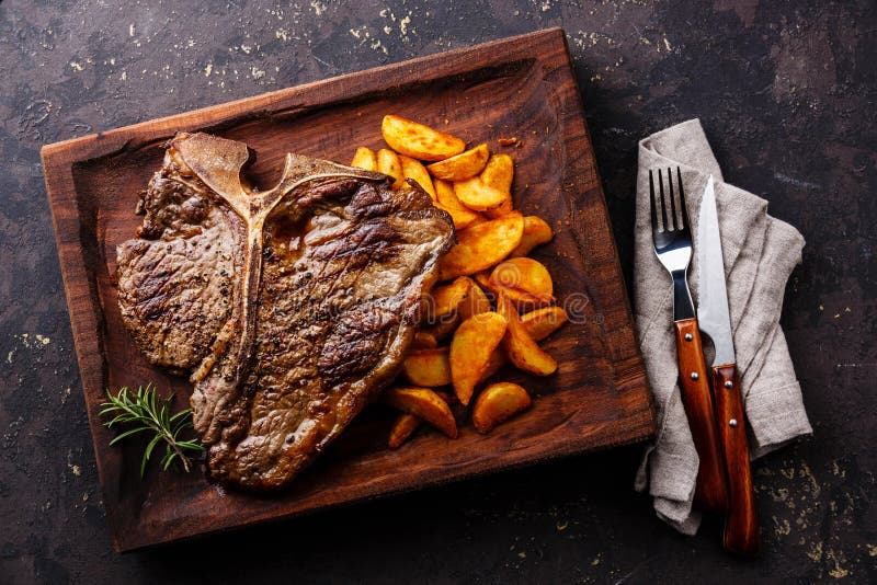 Μέση σπάνια ψημένη στη σχάρα T-Bone μπριζόλα με τις σφήνες πατατών στοκ εικόνα Μέση σπάνια ψημένη στη σχάρα T-Bone μπριζόλα με τις σφήνες πατατών στοκ εικόνα