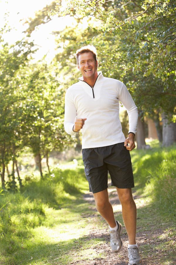 Middle Aged Man Jogging In Park Smiling At Camera. Middle Aged Man Jogging In Park Smiling At Camera