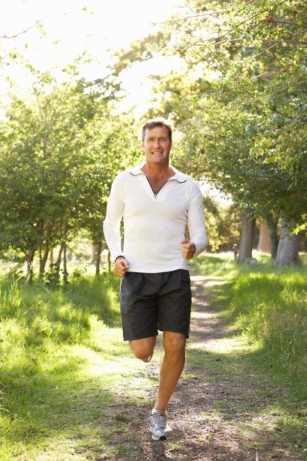 Middle Aged Man Jogging In Park Smiling At Camera. Middle Aged Man Jogging In Park Smiling At Camera