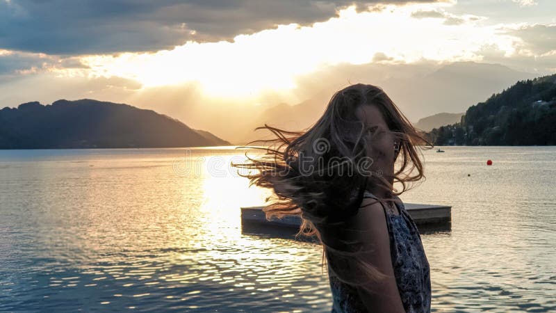 μίλσταετερ μια γυναίκα με μπλε φόρεμα αναστρέφει τα μακριά καστανά μαλλιά της από την ακτή της λίμνης millstaettersee. ο ήλιος δύε στοκ φωτογραφία με δικαίωμα ελεύθερης χρήσης