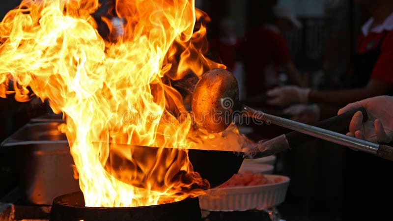 Professional chef in a commercial kitchen cooking flambe style. Chef frying food in flaming pan on gas hob in commercial kitchen. Professional chef in a commercial kitchen cooking flambe style. Chef frying food in flaming pan on gas hob in commercial kitchen.