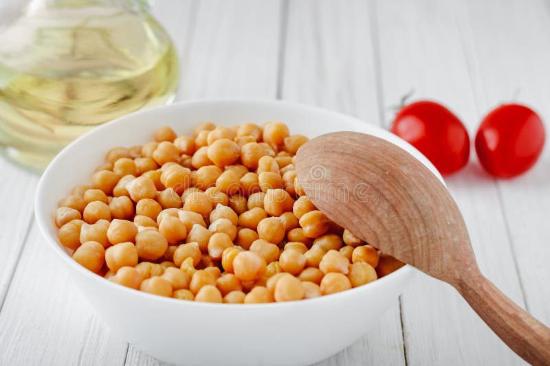 Μαγειρευμένα chickpeas με ένα πιάτο, τις ντομάτες και το ελαιόλαδο σε έναν ξύλινο πίνακα στοκ εικόνα