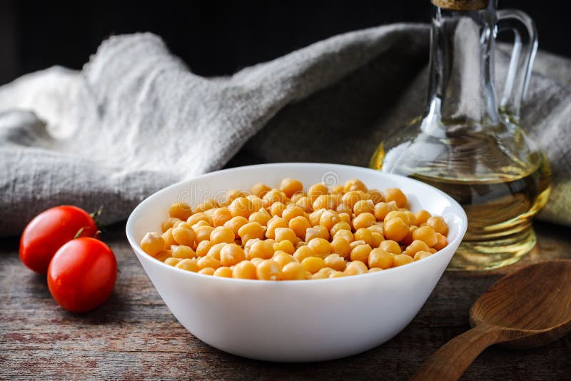 Μαγειρευμένα chickpeas στο πιάτο, τις ντομάτες και το ελαιόλαδο σε έναν ξύλινο πίνακα στοκ φωτογραφία με δικαίωμα ελεύθερης χρήσης