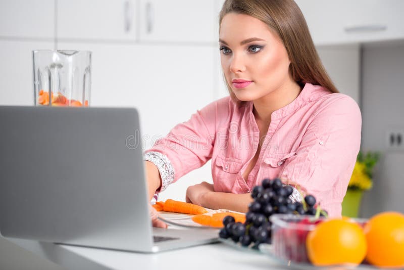 Μαγειρεύοντας γυναίκα που εξετάζει το lap-top προετοιμάζοντας τα τρόφιμα στην κουζίνα στοκ φωτογραφία με δικαίωμα ελεύθερης χρήσης Μαγειρεύοντας γυναίκα που εξετάζει το lap-top προετοιμάζοντας τα τρόφιμα στην κουζίνα στοκ φωτογραφία με δικαίωμα ελεύθερης χρήσης