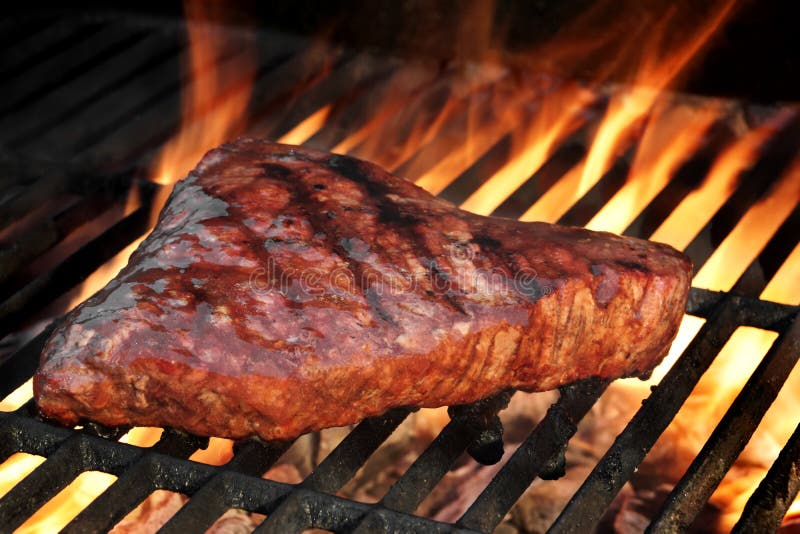 Marinated Beef Steak On The Hot BBQ Charcoal Grill. Flame Of Fire In The Background. Marinated Beef Steak On The Hot BBQ Charcoal Grill. Flame Of Fire In The Background.