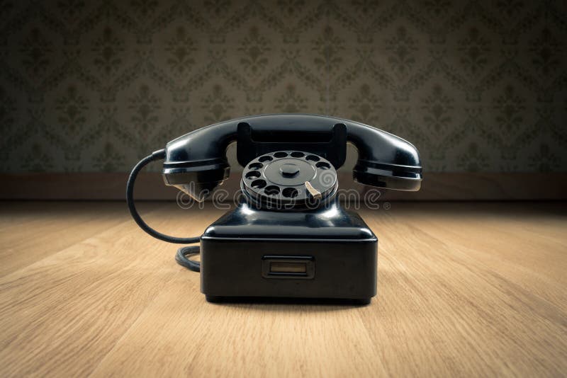 Black 1950s style phone on hardwood floor and vintage wallpaper on background. Black 1950s style phone on hardwood floor and vintage wallpaper on background.