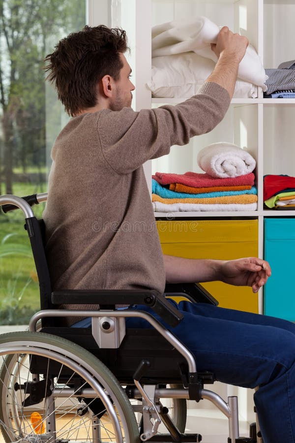 Young disabled man reaching out for blanket at shelf. Young disabled man reaching out for blanket at shelf