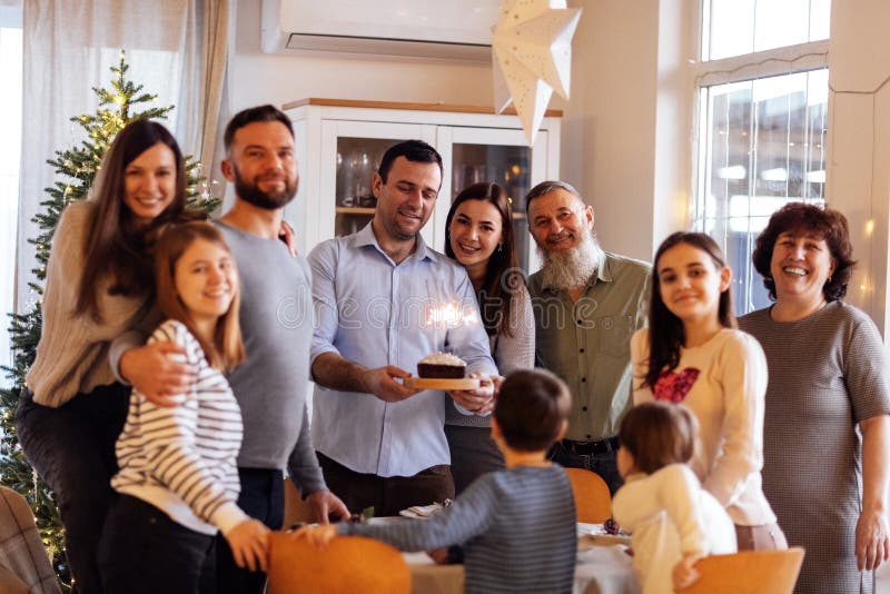 μεγάλη χαρούμενη οικογένεια σε εορταστικό τραπέζι στο σπίτι. ένας ελκυστικός νεαρός με τούρτα με αναμμένα αστεράκια και το χαμόγελ στοκ εικόνες