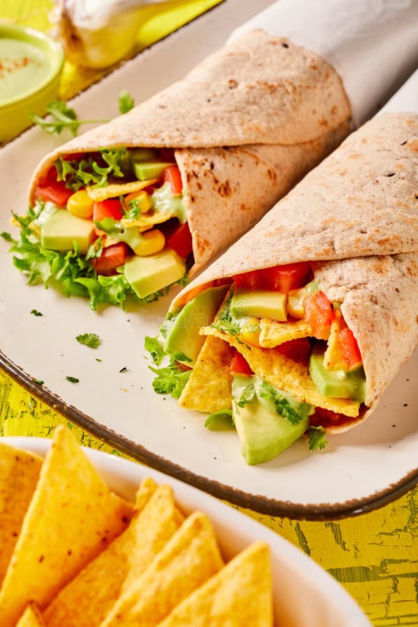 Speciality Mexican tortilla wraps with nachos, fresh avocado pear, chilli peppers and lettuce served on a rectangular platter. Speciality Mexican tortilla wraps with nachos, fresh avocado pear, chilli peppers and lettuce served on a rectangular platter