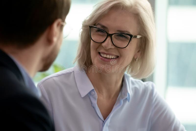 Middle-aged 60s smiling businesswoman talking with partner having pleasant conversation close up focus on female. Negotiations process between client and company manager, mature mentor couch portrait. Middle-aged 60s smiling businesswoman talking with partner having pleasant conversation close up focus on female. Negotiations process between client and company manager, mature mentor couch portrait