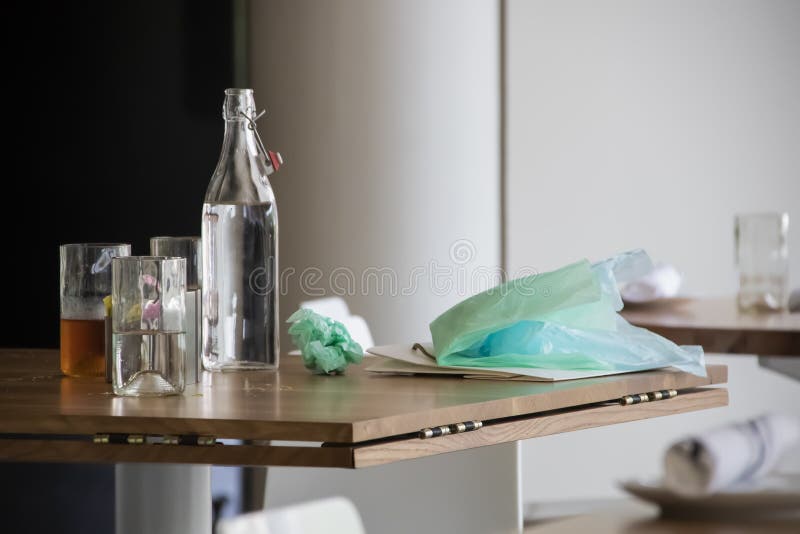 Μετά από το μεσημεριανό γεύμα γενεθλίων - μπουκάλι νερό και γυαλιά που κάθονται στον πίνακα με την εγκαταλειμμένη τσάντα τυλίγοντ στοκ εικόνες Μετά από το μεσημεριανό γεύμα γενεθλίων - μπουκάλι νερό και γυαλιά που κάθονται στον πίνακα με την εγκαταλειμμένη τσάντα τυλίγοντ στοκ εικόνες