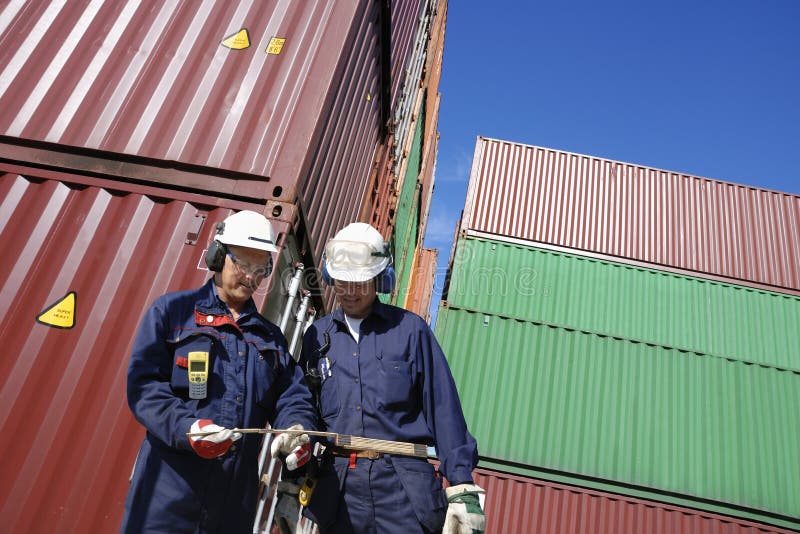 Dock and port workers talking, with stacks of freight containers in background inside commercial container port. Dock and port workers talking, with stacks of freight containers in background inside commercial container port