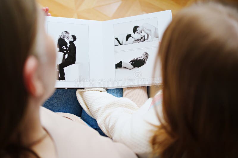 μητέρα και κόρη γυρίζουν μέσα από ένα βιβλίο με φωτογραφίες του μπαμπά και της εγκύου μαμάς. στοκ φωτογραφία