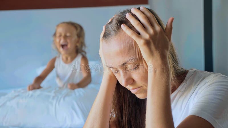 Portrait of upset tired mother with angry little child girl screaming and beating pillow on the background. A hyperactive difficult kids and despairing parents concept. Portrait of upset tired mother with angry little child girl screaming and beating pillow on the background. A hyperactive difficult kids and despairing parents concept.