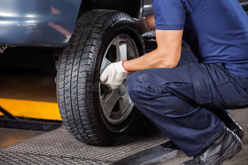 Low section of mechanic fixing car tire at auto repair shop. Low section of mechanic fixing car tire at auto repair shop