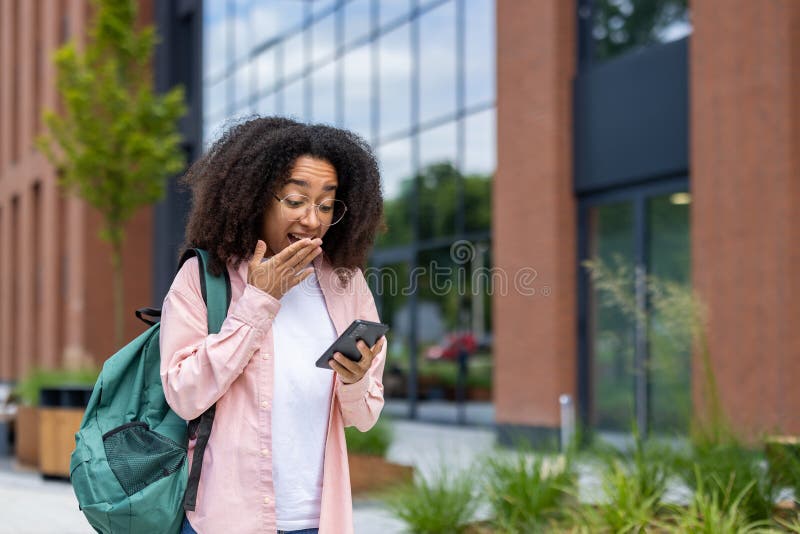 Μια έκπληκτη νεαρή γυναίκα κοιτάζει το smartphone της έξω εκφράζοντας σοκ και καλύπτοντας το στόμα της. στοκ φωτογραφίες