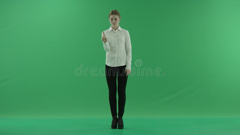 Μια επιχειρηματίας που περνά μέσα από μια εικονική οθόνη μπροστά από ένα πράσινο φόντο Φοράει επίσημο φόρεμα: λευκό πουκάμισο