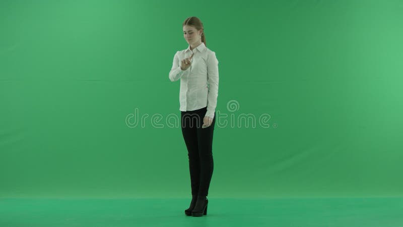 Μια επιχειρηματίας που περνά μέσα από μια εικονική οθόνη μπροστά από ένα πράσινο φόντο Φοράει επίσημο φόρεμα: λευκό πουκάμισο