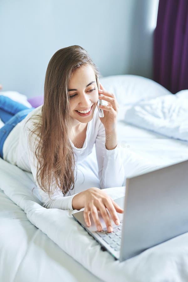 Μια νέα χαμογελώντας γυναίκα με το lap-top που χρησιμοποιεί το τηλέφωνο στοκ φωτογραφία με δικαίωμα ελεύθερης χρήσης Μια νέα χαμογελώντας γυναίκα με το lap-top που χρησιμοποιεί το τηλέφωνο στοκ φωτογραφία με δικαίωμα ελεύθερης χρήσης