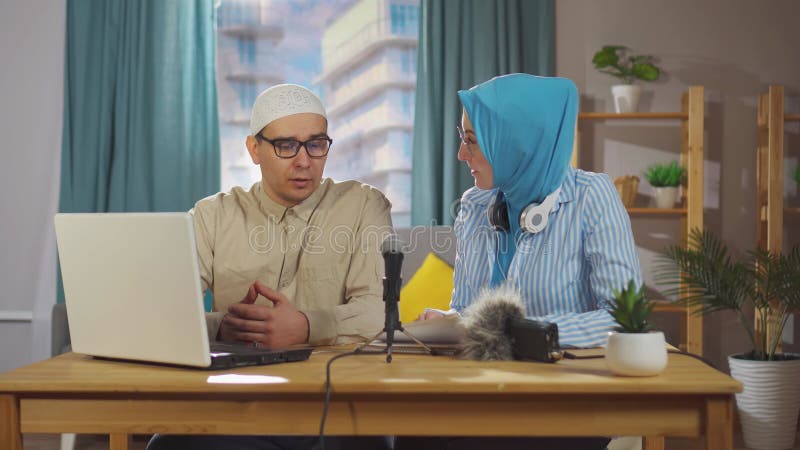 μια νεαρή μουσουλμάνα και ένας μουσουλμάνος καταγράφουν ένα podcast συνέντευξης ενώ κάθονται μπροστά από ένα μικρόφωνο στους ζωντα