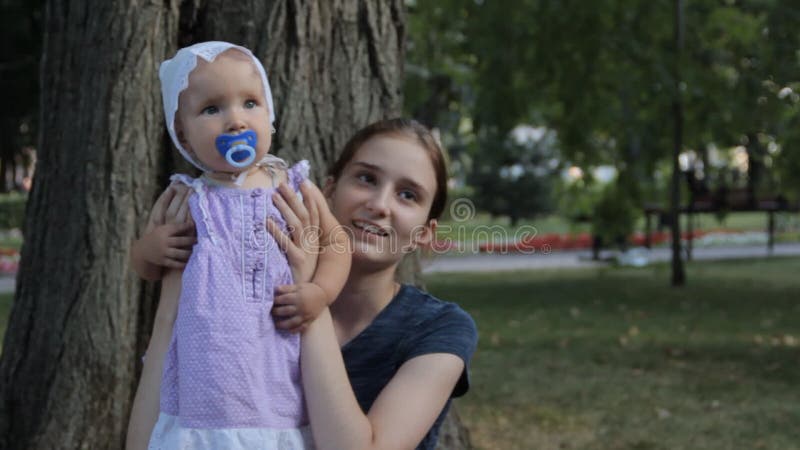 Μια πολύ νέα παραμάνα που έχει ένα κοριτσάκι με ένα soother στην περιτύλιξή της