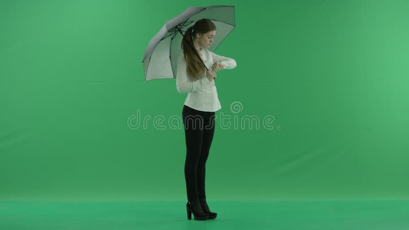 Μια σκεπτόμενη γυναίκα περιμένει και την κοιτάζει να στέκεται δεξιά με την ομπρέλα πάνω από την πράσινη οθόνη Φοράει επίσημα