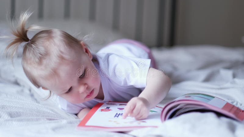 μικρό κοριτσάκι που διαβάζει φωτογραφίες στο κρεβάτι στο σπίτι ένα παράξενο μωρό θέλει να διαβάσει ένα νέο παραμύθι.