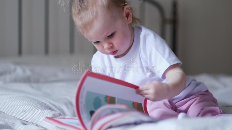 μικρό κοριτσάκι που διαβάζει φωτογραφίες στο κρεβάτι στο σπίτι ένα παράξενο μωρό θέλει να διαβάσει ένα νέο παραμύθι.