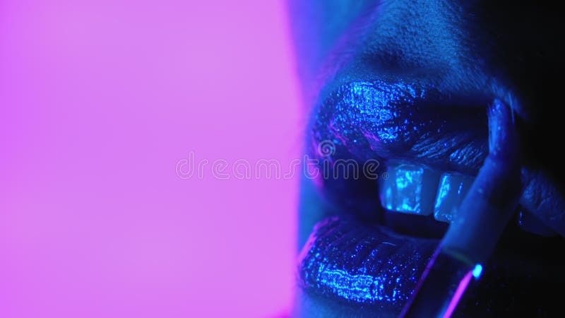μοντέλο μόδας που εφαρμόζει γυαλιστερά στιλπνά ή κραγιόν σε στολισμένα σαγόνια. φως neon studio. μακροεντολή της γυναίκας
