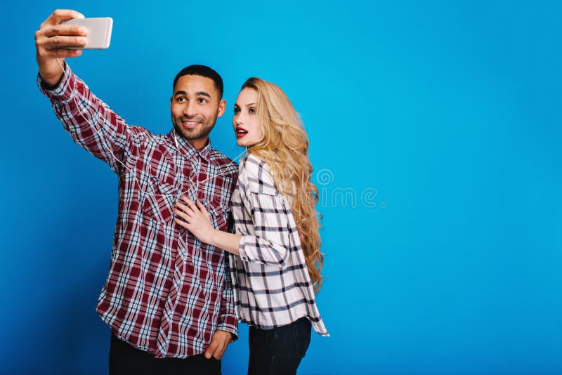Μοντέρνος όμορφος τύπος που κάνει selfie το πορτρέτο με την ελκυστική νέα γυναίκα με τη μακριά ξανθή τρίχα στο μπλε υπόβαθρο Έχον στοκ φωτογραφία με δικαίωμα ελεύθερης χρήσης Μοντέρνος όμορφος τύπος που κάνει selfie το πορτρέτο με την ελκυστική νέα γυναίκα με τη μακριά ξανθή τρίχα στο μπλε υπόβαθρο Έχον στοκ φωτογραφία με δικαίωμα ελεύθερης χρήσης