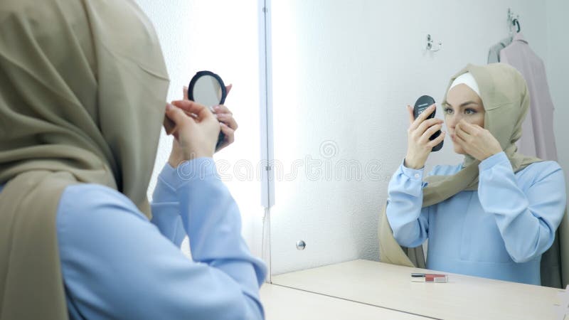 Μουσουλμανική νέα ελκυστική γυναίκα στο μπεζ hijab και το παραδοσιακό μπλε φόρεμα που κάνει τη σύνθεση
